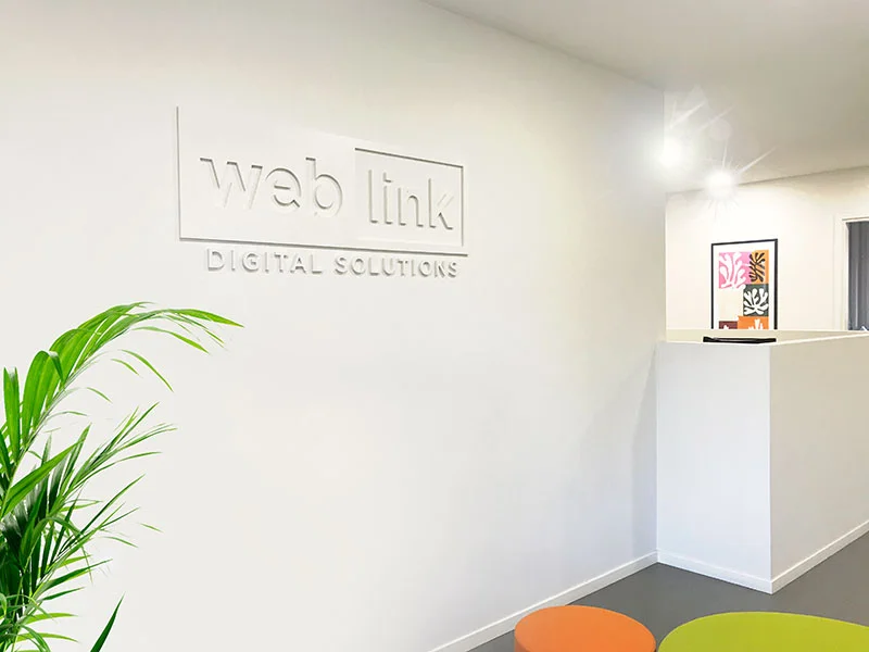 weblink-welcome.jpg Interno dell'ufficio di Web Link, con logo e piante ornamentali in un ambiente luminoso e moderno.